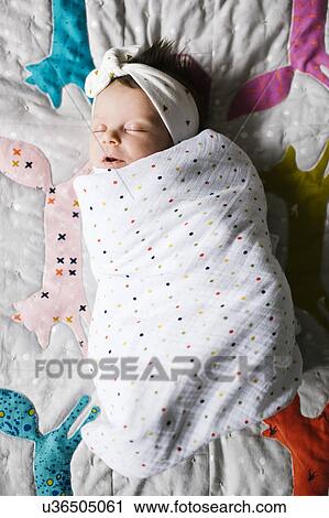 Stock Image - Baby girl (0-1 months) wrapped in blanket sleeping on bed. Fotosearch