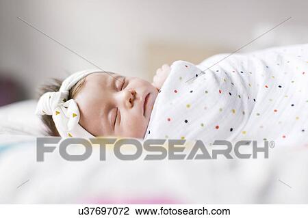 Stock Image - Baby girl (0-1 months) wrapped in blanket sleeping on bed. Fotosearch