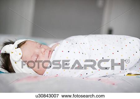 Stock Photo - Baby girl (0-1 months) wrapped in blanket sleeping on bed. Fotosearch