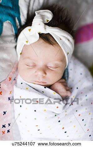 Stock Photo - Baby girl (0-1 months) wrapped in blanket sleeping on bed. Fotosearch