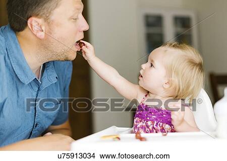 Picture - Baby girl (12-17 months) feeding her father. Fotosearch