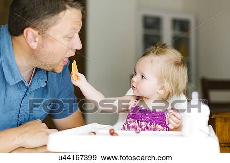 Stock Photo - Baby girl (12-17 months) feeding her father. Fotosearch
