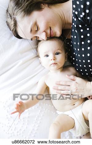 Stock Image - Baby girl (6-11 Months) being hugged by mother, directly above. Fotosearch