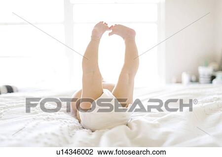 Stock Image - Baby girl (6-11 Months) lying down on bed with feet in air. Fotosearch