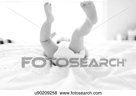 Stock Photo - Baby girl (6-11 Months) lying down on bed with feet in air. Fotosearch