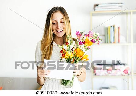 Stock Photo - Beautiful woman reading letter and holding flowers. Fotosearch