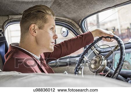 Stock Image - Blond man driving vintage car. Fotosearch