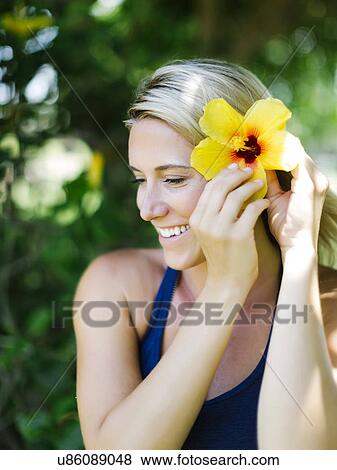 Stock Photo - Blonde beautiful woman decorates hair with flower. Fotosearch
