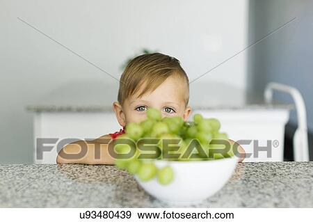 Stock Photo - Boy (2-3) hiding behind bowl with grapes. Fotosearch