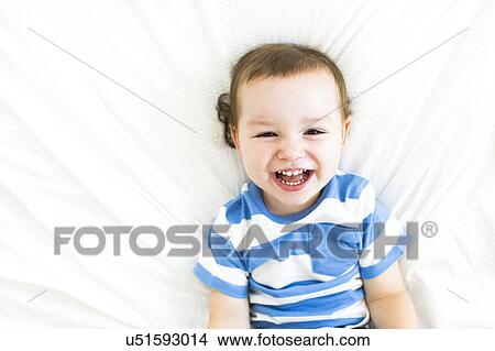 Picture - Boy (4-5) lying on bed and laughing. Fotosearch