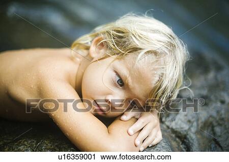 Stock Image - Boy (4-5) resting on rocks. Fotosearch