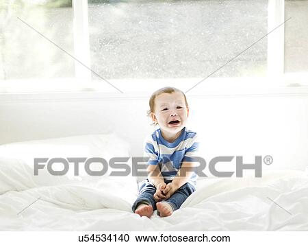 Stock Image - Boy (4-5) sitting on bed and crying. Fotosearch