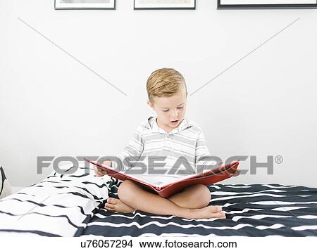 Picture - Boy (4-5) sitting on bed and reading book. Fotosearch