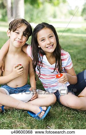 Boy (6-7) and girl (10-11) sitting on grass in summer View Large Photo Image Stock Photo - Boy (6-7) and girl (10-11) sitting on grass in summer. Fotosearch