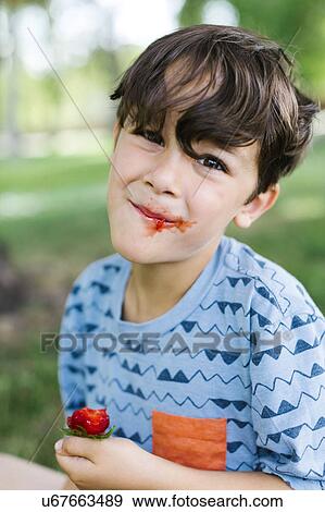 Boy (6-7) eating strawberry in park View Large Photo Image Stock Photo - Boy (6-7) eating strawberry in park. Fotosearch