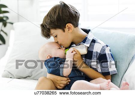 Stock Photography - Boy( 6-7) feeding small brother (12-17 months). Fotosearch