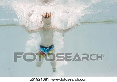 Stock Image - Boy (6-7) jumping into swimming pool. Fotosearch