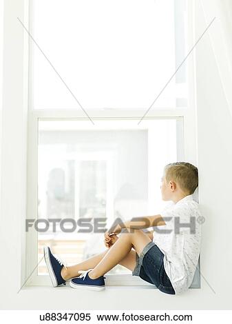 Stock Photography - Boy (6-7) looking through window. Fotosearch