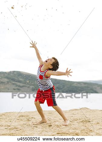 Boy (6-7) playing on beach by lake View Large Photo Image Picture - Boy (6-7) playing on beach by lake. Fotosearch