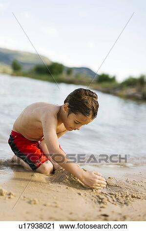 Stock Image - Boy (6-7) playing on beach by lake. Fotosearch