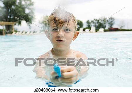 Picture - Boy (6-7) playing with squirt gun in swimming pool. Fotosearch