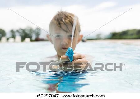 Stock Photo - Boy (6-7) playing with squirt gun in swimming pool. Fotosearch