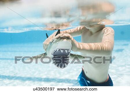 Stock Photo - Boy (6-7) playing with toy shark in swimming pool. Fotosearch