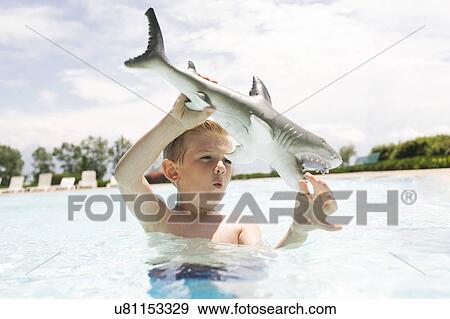 Boy (6-7) playing with toy shark in swimming pool View Large Photo Image Stock Photo - Boy (6-7) playing with toy shark in swimming pool. Fotosearch