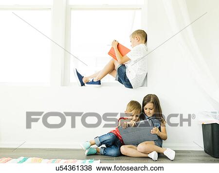 Boy (6-7) reading book and sister with brother (2-3, 6-7) using digital tablet View Large Photo Image Stock Photo - Boy (6-7) reading book and sister with brother (2-3, 6-7) using digital tablet. Fotosearch