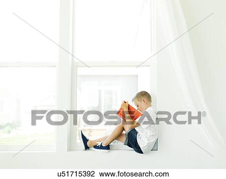 Boy (6-7) reading book by window View Large Photo Image Stock Image - Boy (6-7) reading book by window. Fotosearch