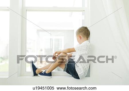 Stock Photography - Boy (7-8) looking through window. Fotosearch