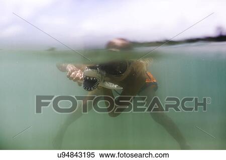Stock Photography - Boy (8-9) playing with toy shark in sea. Fotosearch