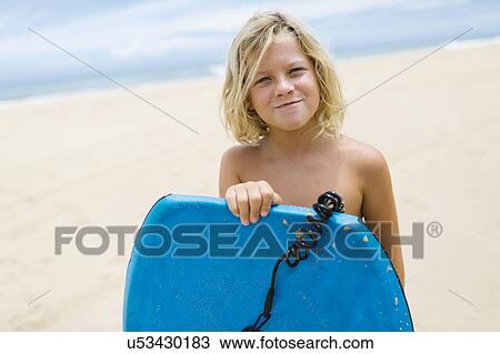 Boy (8-9) standing on beach and holding surfboard View Large Photo Image Stock Image - Boy (8-9) standing on beach and holding surfboard. Fotosearch