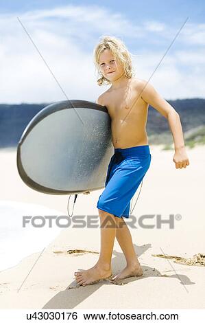 Boy (8-9) standing on beach and holding surfboard View Large Photo Image Stock Photograph - Boy (8-9) standing on beach and holding surfboard. Fotosearch