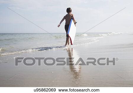 Boy (8-9) walking and carrying body board in empty beach View Large Photo Image Stock Photo - Boy (8-9) walking and carrying body board in empty beach. Fotosearch