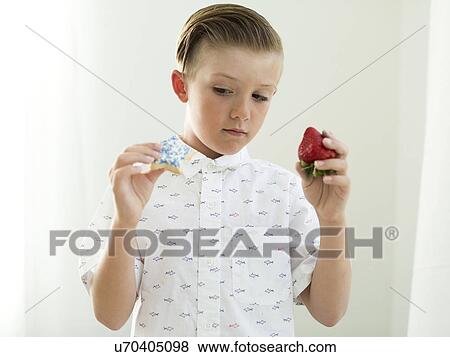 Stock Photo - Boys (6-7) holding strawberry and cookie in hands. Fotosearch