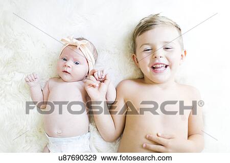 Stock Photo - Brother (4-5) and sister (0-1 months) lying on bed. Fotosearch