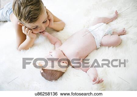 Stock Photograph - Brother (4-5) and sister (0-1 months) lying on bed. Fotosearch