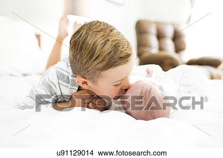 Brother (4-5) lying on bed and kissing sister (0-1 months) View Large Photo Image Picture - Brother (4-5) lying on bed and kissing sister (0-1 months). Fotosearch