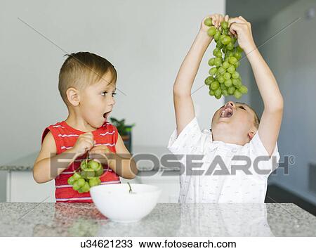 Stock Image - Brothers (2-3, 6-7) eating white grapes. Fotosearch
