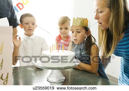 Stock Photo - Brothers (2-3, 6-7) looking at sister (6-7) and mother blowing birthday candles. Fotosearch