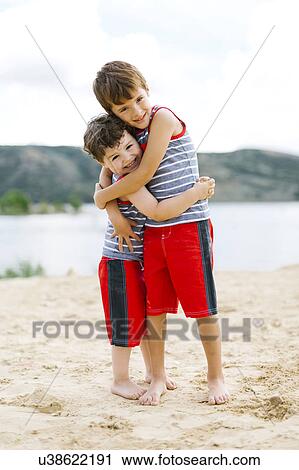 Stock Image - Brothers (4-5, 6-7) embracing on beach by lake. Fotosearch