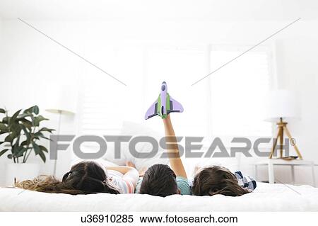 Brothers ( 6-7, 8-9 ) and sister ( 10-11 ) lying on bed and playing with toy View Large Photo Image Stock Photography - Brothers ( 6-7, 8-9 ) and sister ( 10-11 ) lying on bed and playing with toy. Fotosearch