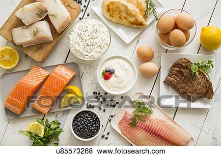 Stock Photo - Chicken meat, fish, cottage cheese, yogurt and eggs on white table. Fotosearch
