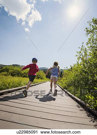 Stock Image - Children (4-5) running on boardwalk. Fotosearch