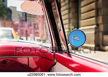 Stock Image - Cuba, Havana, Cuban flag reflecting in mirror of convertible. Fotosearch