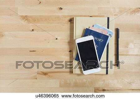 Stock Photography - Diary, passport with paper currency, smart phone and pen on wooden table. Fotosearch