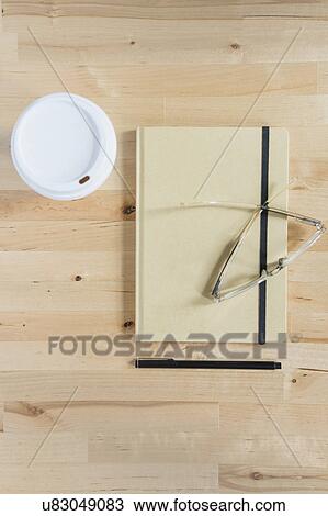 Stock Image - Disposable cup, diary, eyeglasses and pen on wooden desk. Fotosearch