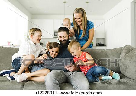 Stock Image - Family with four children (6-11 months, 2-3, 6-7) using digital tablet. Fotosearch