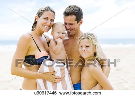 Stock Photograph - Family with two children (12-17 months, 8-9) embracing on beach. Fotosearch